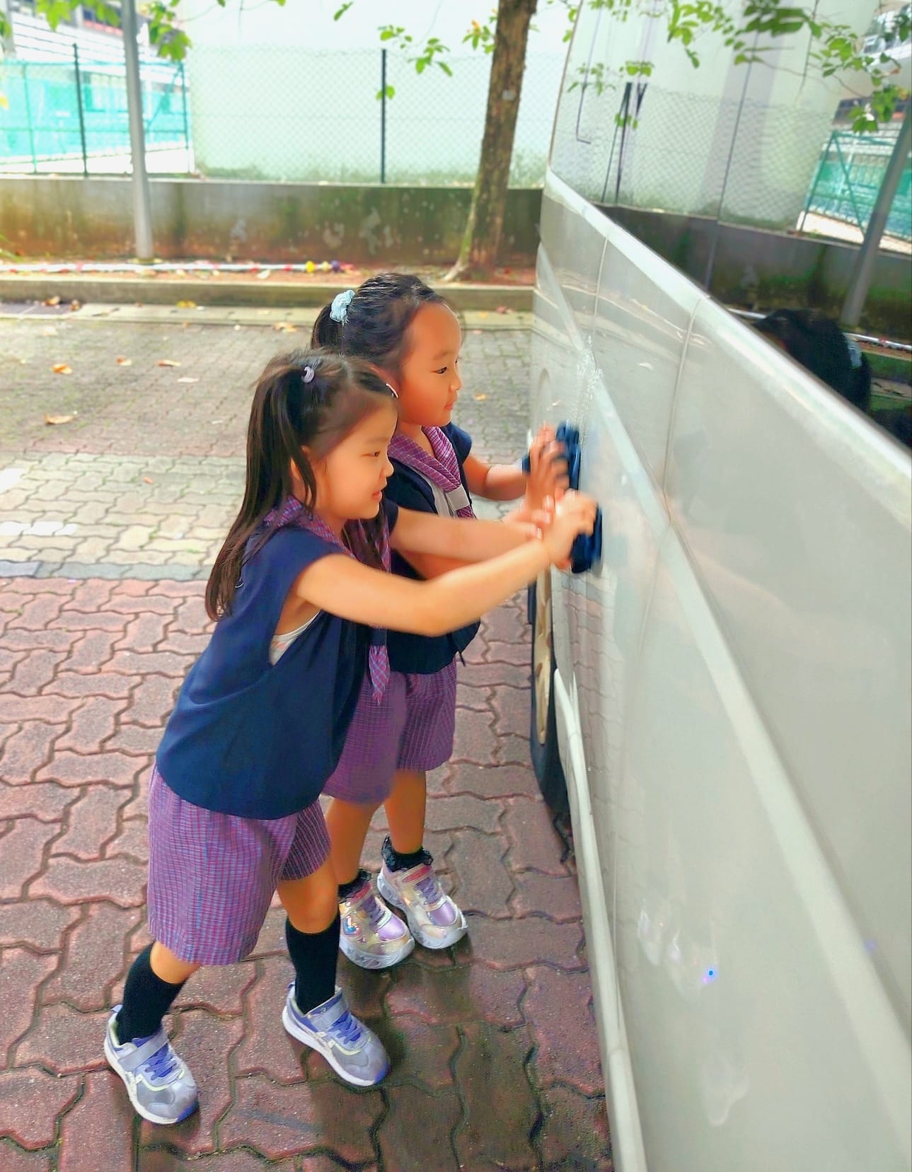 Two Arts Junior children washing a vehicle together outdoors